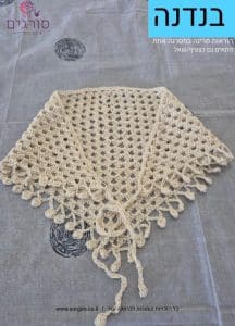 Beige crochet shawl with an open lattice pattern and fringed scalloped edge laid flat on a gray surface.
